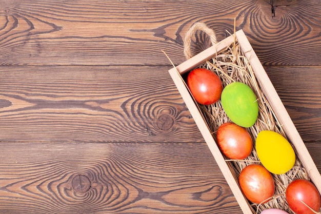 Top view of Easter colorful eggs on a bed of straw in a long wooden box on a wooden table and space for text