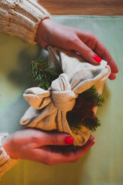 Vista dall'alto di un regalo di natale ecologico decorato con materiali naturali una donna tiene un regalo avvolto in tessuto naturale e decorato con un ramo di abete