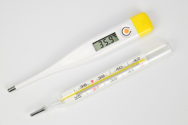 top view of electronic and mercury thermometers lying side by side on a white background