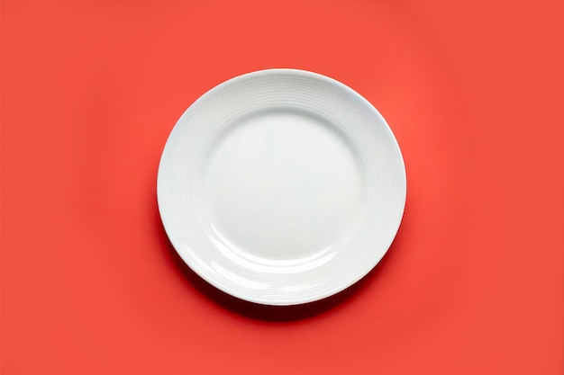 Фото Вид сверху пустая пустая керамическая круглая белая тарелка, изолированная на пастельно-красном фоне с обтравочным контуром