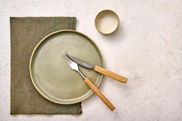 Piatto verde vuoto di vista superiore con il tovagliolo e la casseruola del coltello della forchetta sul disegno strutturato bianco del fondo