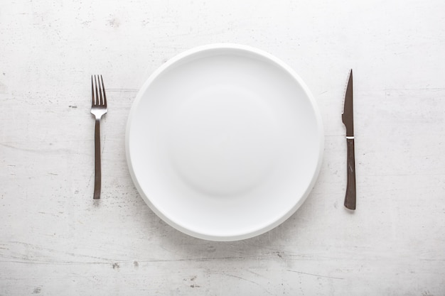 Top of view empty plate with fork and knife on white concrete background.