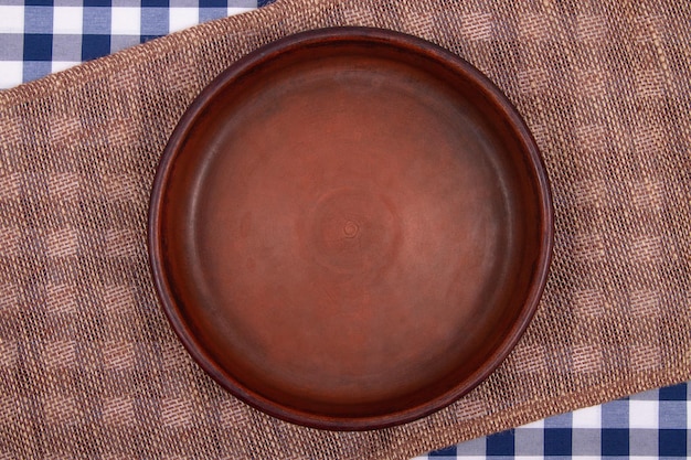 Top view of Empty round clay pan on table covered with checkered tablecloth and sacking napkin