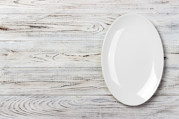 Top view of empty white food plate on a wood background