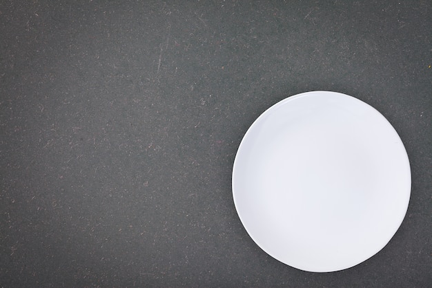 Top view of an empty white plate placed on a blackboard with copy space.