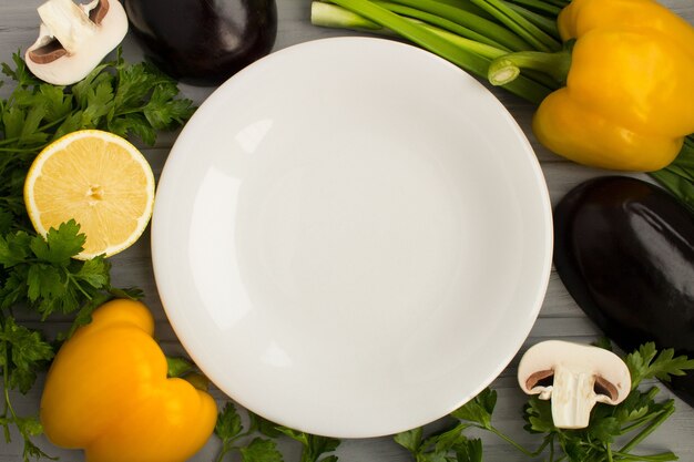 Top view of empty white plate, vegetables and fruit on the grey wooden