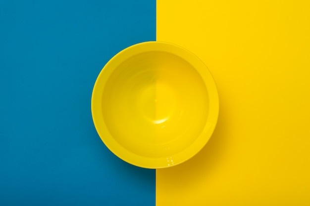 Top view of an empty yellow bowl on a yellow and blue background. Plastic utensils for the kitchen.