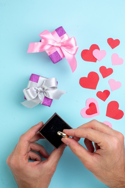 top view engagement ring box in male hands red and pink hearts gifts on blue background