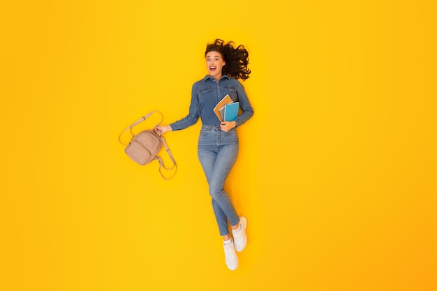 Top view of enthusiastic student woman grasping backpack yellow backdrop