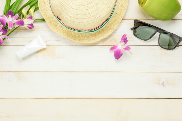 Top view essential travel summer items.The sunblock moisturizing  hat  sunglasses orchid on white  wooden background.