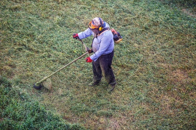 Top view fat dirty lawnmover man worker cutting dry grass with lawn mower