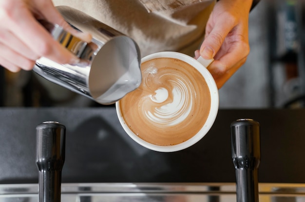 Vista dall'alto del barista femminile che utilizza il latte per decorare la tazza di caffè