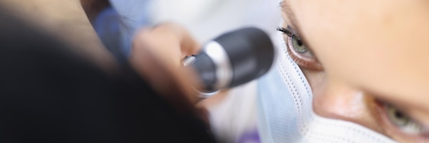 Top view of female ent doctor in medical mask examining ear with otoscope carefully