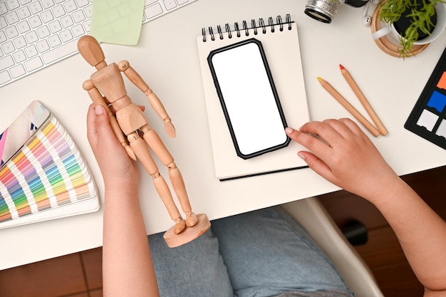 Top view Female graphic designer holding a wood human figure and using smartphone