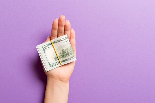 Top view of female hand holding a lot of rolled up dollar banknotes on colorful background. Poverty concept. Credit concept with copy space