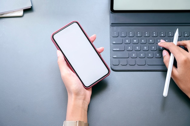 Top view female hand holding smartphone with blank screen and working with tablet.