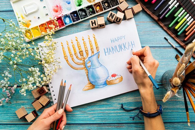 Top view of female hands drawing a watercolor art Happy Hanukkah