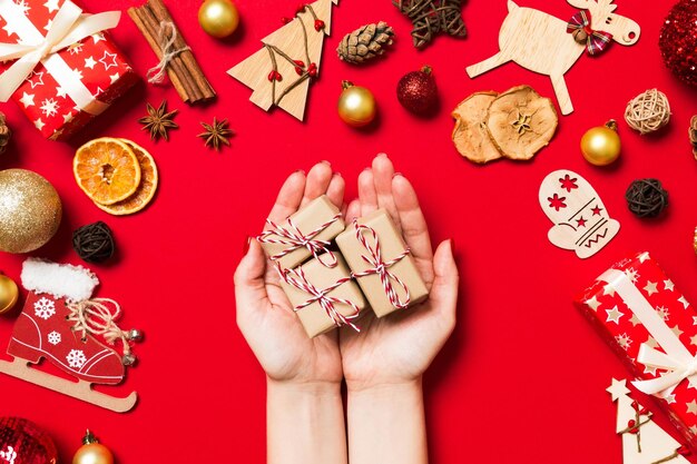 Foto vista dall'alto delle mani femminili che tengono un regalo di natale su sfondo rosso festivo decorazioni natalizie concetto di vacanza di capodanno