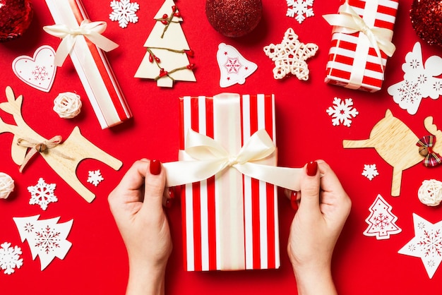 Top view of female hands holding a Christmas present on festive red background Holiday decorations New Year holiday concept