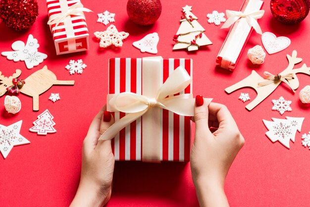 Top view of female hands holding a Christmas present on festive red background