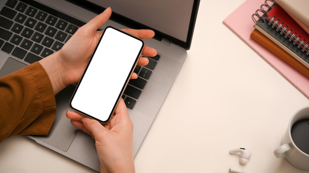 上面図現代のオフィスデスクのスマートフォンの空白の画面上に彼女の携帯電話を保持している女性の手
