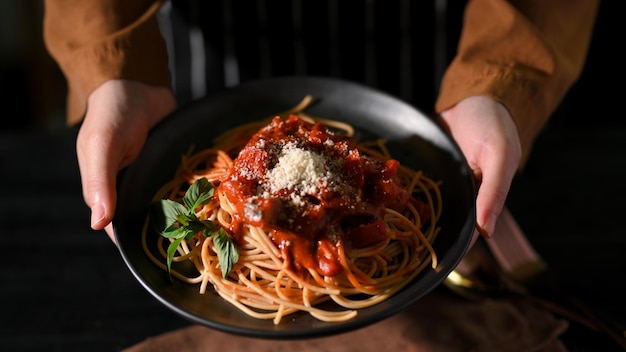 Vista dall'alto mani femminili che tengono o servono un piatto di spaghetti italiani con salsa di pomodoro speciale