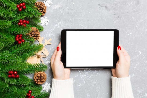 Top view female hands holding a tablet on cement Christmas  made fir tree and festive decorations.   holiday . Mockup