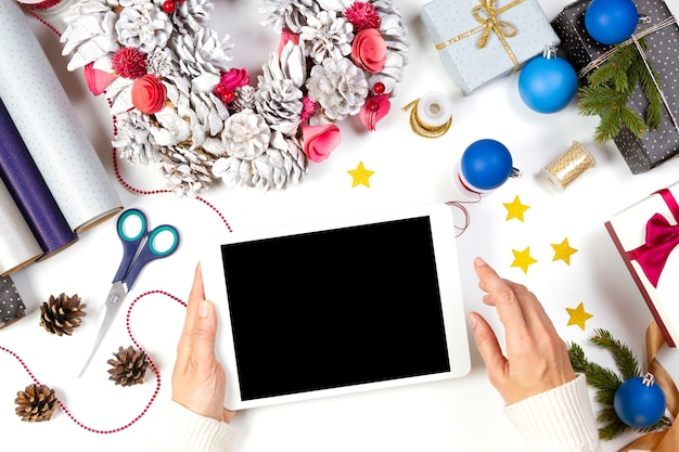 Top view to female hands holding tablet computer over white table with Christmas present gift boxes