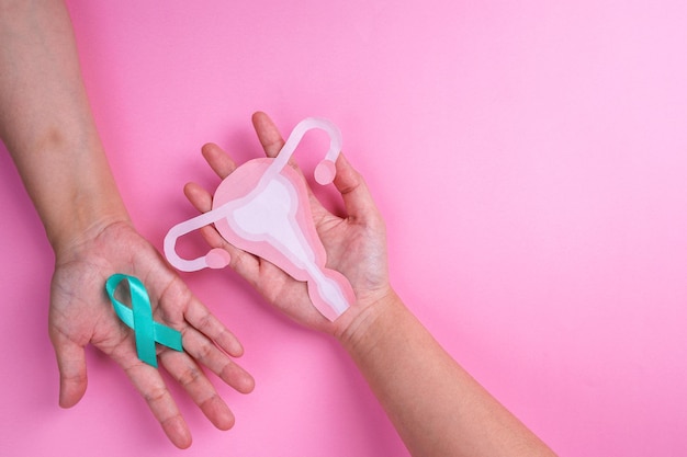 Photo top view of female hands holding teal ribbon and uterus cutout ovarian cancer concept