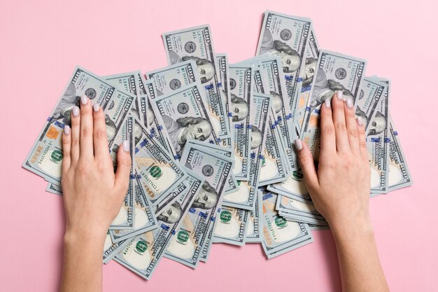 Top view of female hands lying on a pile of one hundred dollar banknotes. Success and wealth concept on colorful background.