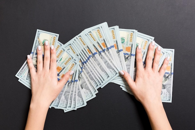 Верхний вид женских рук, лежащих на куче стодолларовых банкнот Концепция успеха и богатства на красочном фоне