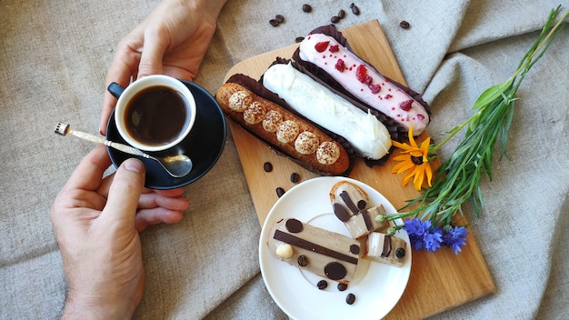 Top view female hands pass a cup of black coffee to a man against the background served eclairs