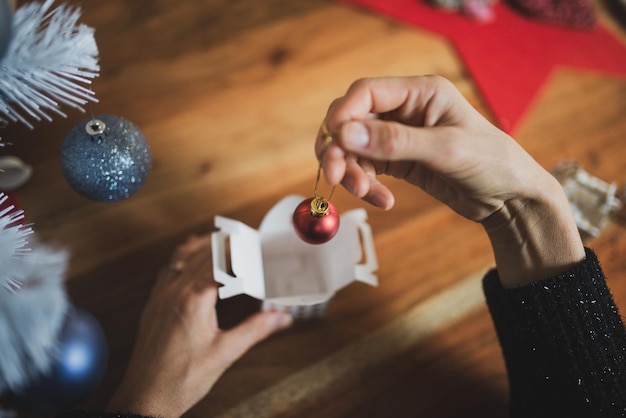 Top view of female hands placing small shiny red holiday bauble in a gift box