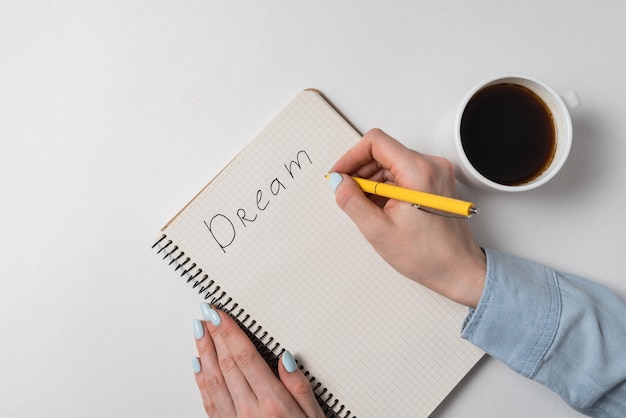 Top view of female hands with notebook and Cup of coffee. Handwritten inscription Dream