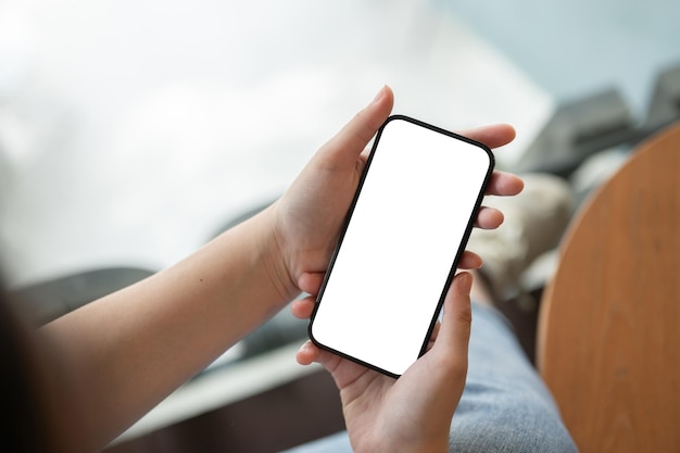 Top view of a female holding a smartphone white screen mockup over a blurred background