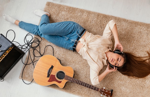 Vista dall'alto del musicista femminile sul pavimento a casa con le cuffie e la chitarra acustica