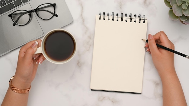 Top view a female working at her desk writing something on notepad on white marble desk background