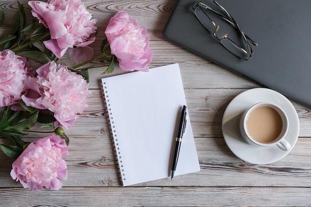 Top view of feminine workspace with laptop blank notepad cup of coffee and peonies flowers