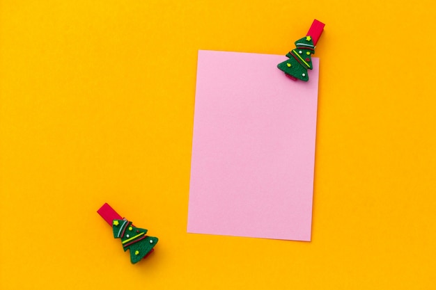 Top view festive christmas clothespins and pink empty paper sheet with free space for text on a vibrant yellow background