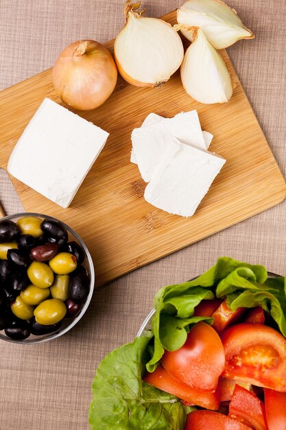 Vista dall'alto del formaggio bianco feta su tavola di legno su un tavolo con olive, insalata estiva e cipolle tagliate