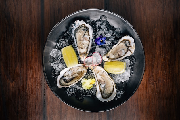 Top view of Fine de Claire Oyster and lemon served in black bowl with ice on wooden table.