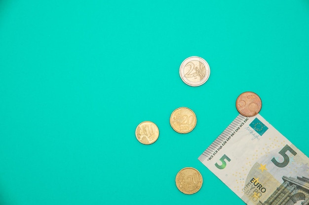 Top view of a five euro banknote and coins on the down right corner on a turquoise background