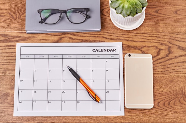 Foto calendario piatto con vista dall'alto con smartphone e libro con penna con occhiali e vaso con pianta