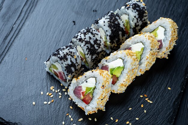 Top view flat lay sushi roll on dark stone plate on dark wall with copy space. Roll with tuna and cream cheese. Seafood. Dunk sushi in soy sauce. Concept of Asian cuisine