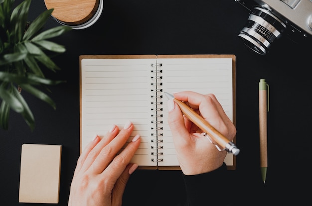 Top view of a flat lay womans hand writes a note in an open notebook lying on a black table next to the camera with a pen and writing paper. The concept of home accounting. Advertising space