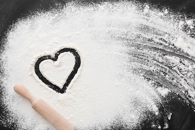Top view of flour with heart shape and rolling pin