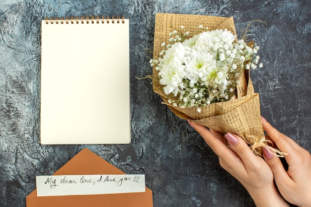 top view flower bouquet in female hands love letter notebook on dark background