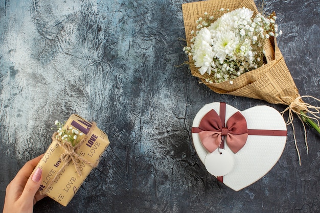 top view flower bouquet heart shaped box gift in female hand on dark background copy place