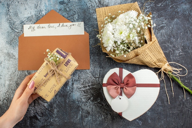 Vista dall'alto bouquet di fiori a forma di cuore scatola regalo in mano femminile lettera d'amore su sfondo scuro