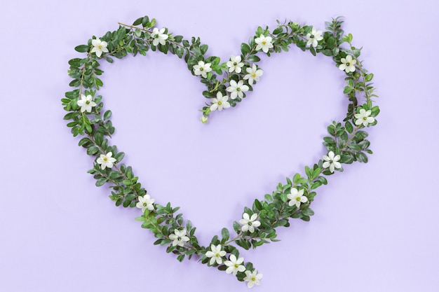 라일락 배경에 야생화, 꽃 봉 오리와 잎으로 만든 꽃 하트 프레임의 상위 뷰. 사랑 개념, 평평하다.